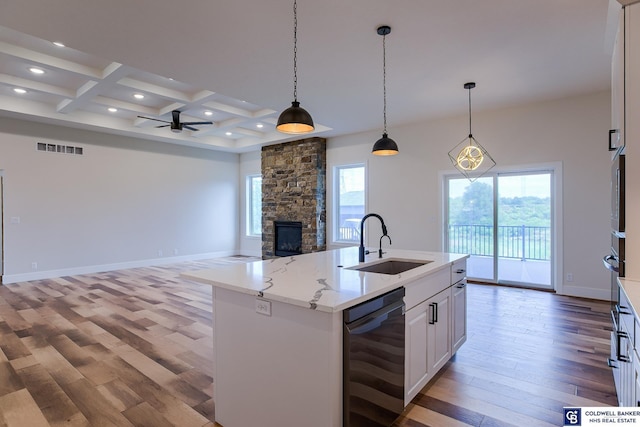 kitchen with coffered ceiling, a kitchen island with sink, sink, white cabinets, and hanging light fixtures