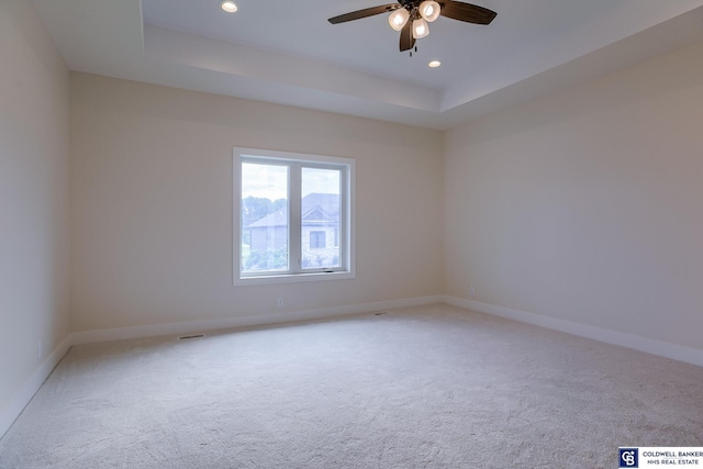 empty room with light colored carpet, a raised ceiling, and ceiling fan