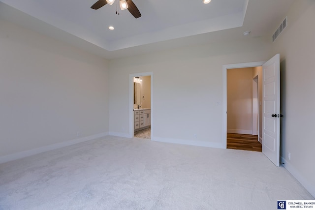 unfurnished bedroom with connected bathroom, light colored carpet, a raised ceiling, and ceiling fan