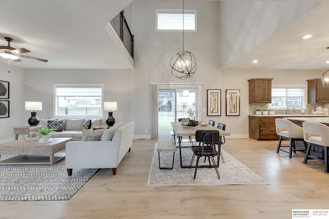 dining area with a towering ceiling, a healthy amount of sunlight, ceiling fan with notable chandelier, and light hardwood / wood-style floors