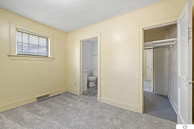 unfurnished bedroom featuring carpet flooring, a textured ceiling, ensuite bath, and a closet