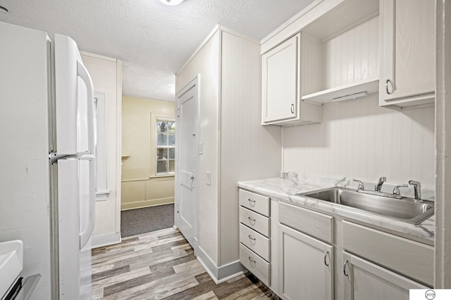 kitchen with sink, light stone counters, light hardwood / wood-style flooring, white refrigerator, and a textured ceiling