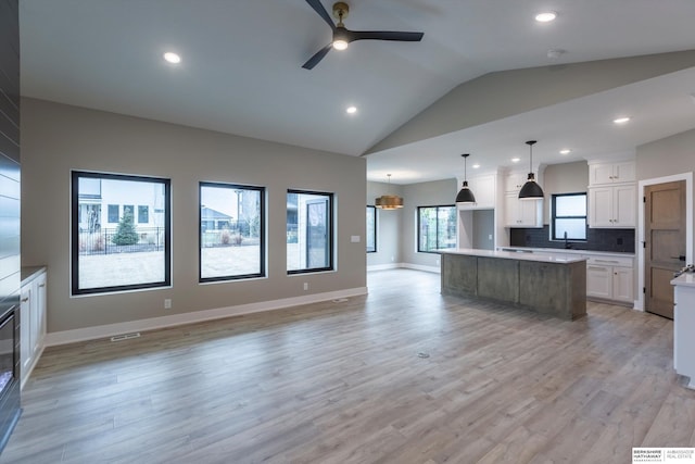 kitchen with pendant lighting, white cabinets, light wood-type flooring, tasteful backsplash, and a kitchen island