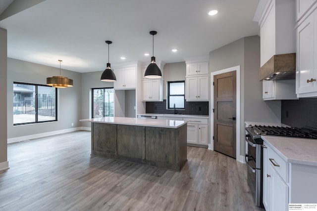 kitchen featuring gas range, sink, a center island, white cabinetry, and hanging light fixtures