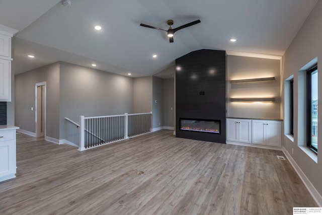 unfurnished living room with light wood-type flooring, built in shelves, ceiling fan, a fireplace, and lofted ceiling