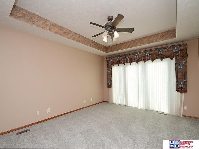 carpeted spare room with a textured ceiling, a raised ceiling, and ceiling fan