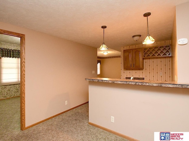 kitchen with light carpet, hanging light fixtures, and a textured ceiling