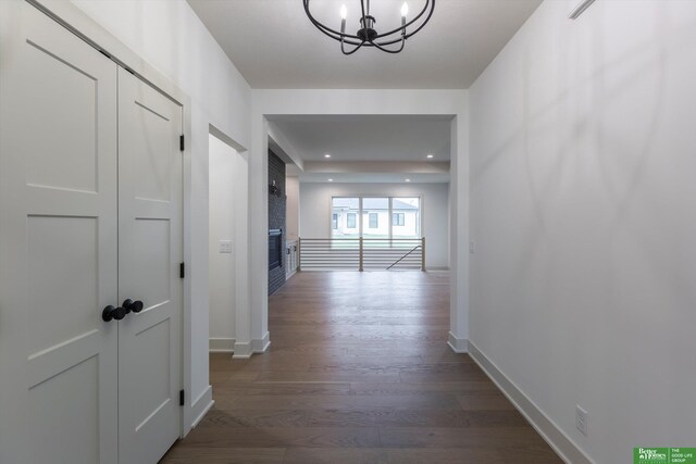 hall with dark wood-style flooring, a notable chandelier, and baseboards