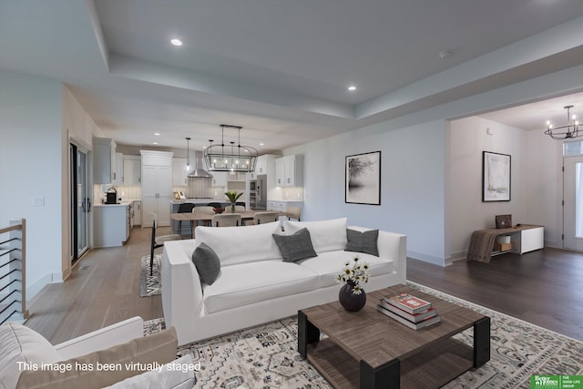 living room with a chandelier, light wood-style flooring, recessed lighting, baseboards, and a raised ceiling