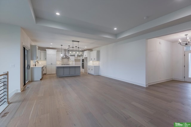 unfurnished living room with a tray ceiling, light hardwood / wood-style flooring, a notable chandelier, and sink