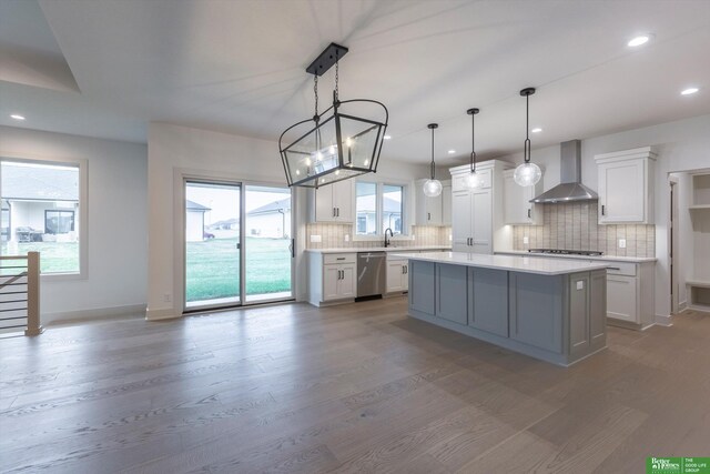 kitchen featuring stainless steel appliances, light countertops, backsplash, wall chimney range hood, and wood finished floors