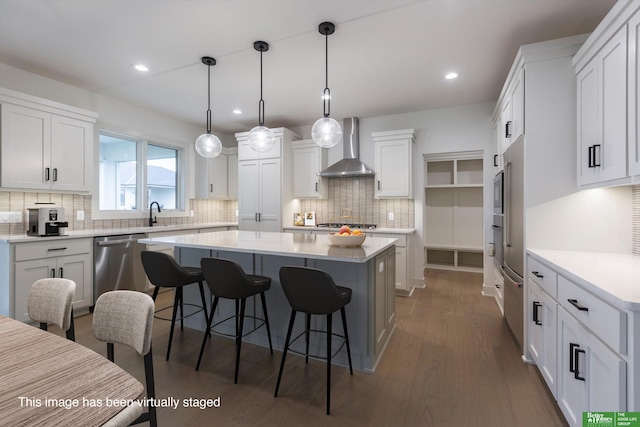 kitchen with white cabinets, wall chimney exhaust hood, stainless steel appliances, and decorative light fixtures