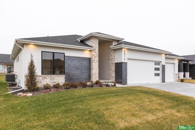 prairie-style house featuring an attached garage, central air condition unit, concrete driveway, stone siding, and a front lawn