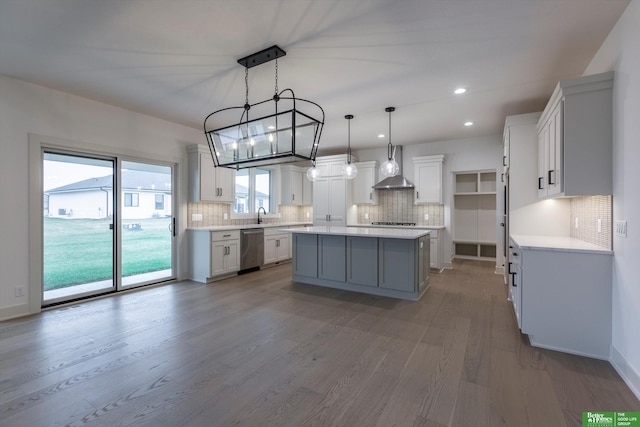 kitchen featuring wood finished floors, a kitchen island, light countertops, wall chimney range hood, and appliances with stainless steel finishes