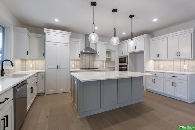 kitchen featuring sink, wall chimney exhaust hood, decorative light fixtures, a kitchen island, and white cabinetry