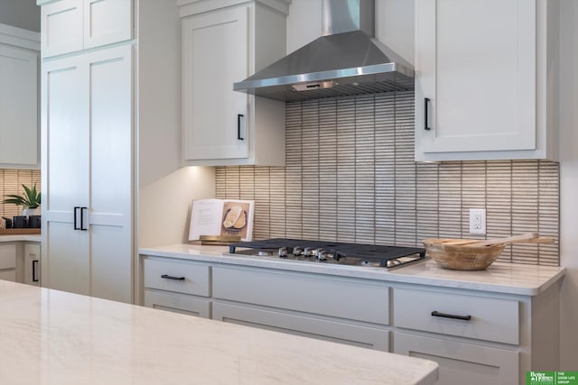 kitchen with white cabinetry, backsplash, light stone countertops, wall chimney exhaust hood, and stainless steel gas stovetop