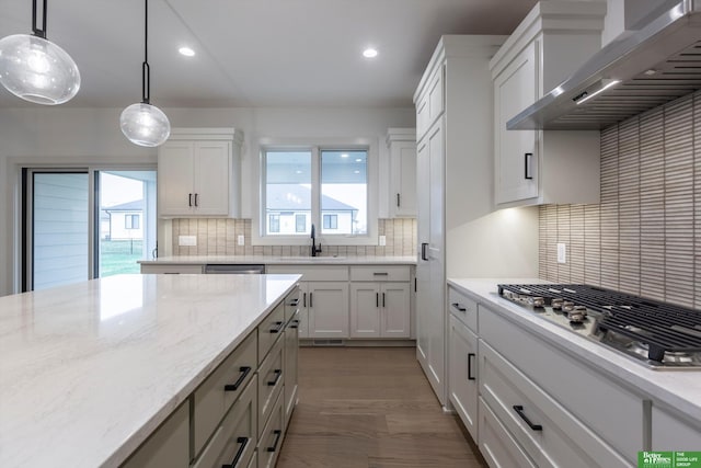 kitchen featuring wall chimney range hood, stainless steel gas stovetop, white cabinetry, and light stone counters