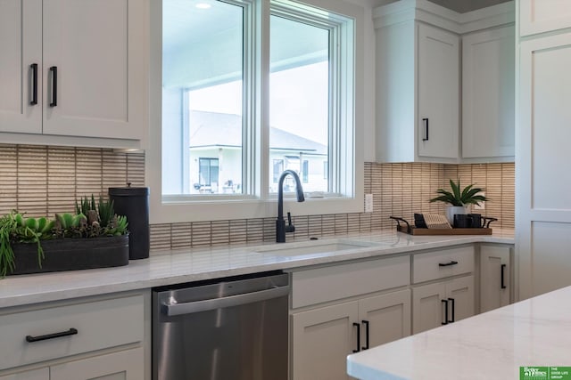 kitchen with stainless steel dishwasher, light stone counters, white cabinets, and sink