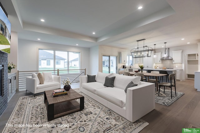 living room with a tray ceiling, a fireplace, a chandelier, and dark hardwood / wood-style floors