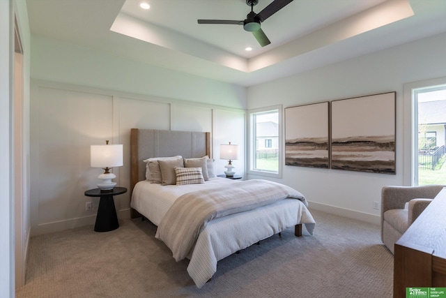 carpeted bedroom with ceiling fan and a raised ceiling