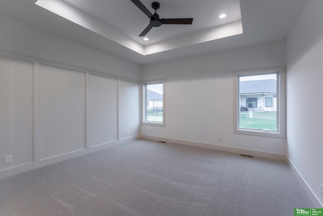 empty room featuring light carpet, a tray ceiling, and ceiling fan