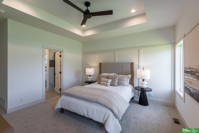 bedroom with a tray ceiling, connected bathroom, ceiling fan, and light carpet