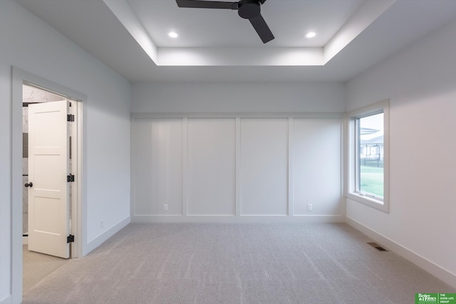 spare room featuring light carpet, a tray ceiling, visible vents, and baseboards