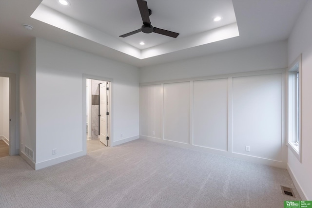 unfurnished bedroom featuring connected bathroom, ceiling fan, a tray ceiling, light carpet, and a closet