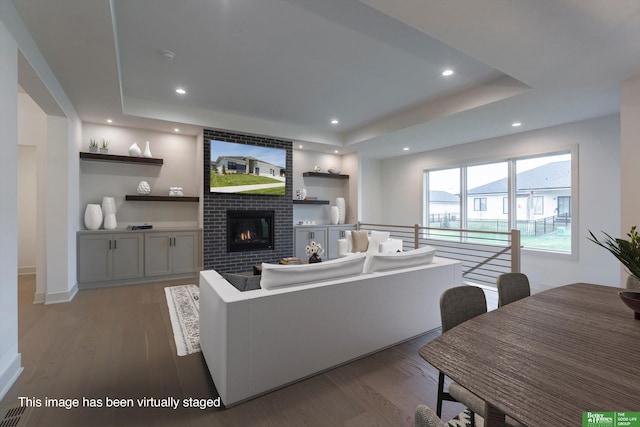 living room featuring wood finished floors, a fireplace, a raised ceiling, and recessed lighting