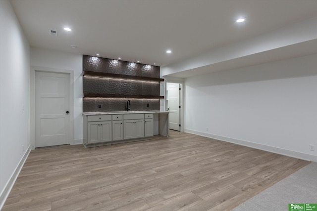 interior space featuring gray cabinetry, sink, backsplash, and light hardwood / wood-style flooring