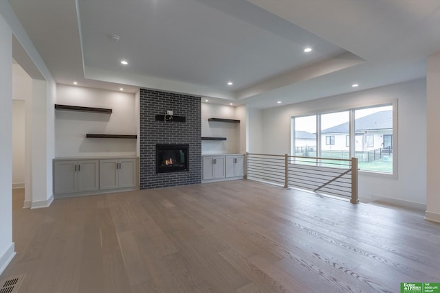 unfurnished living room featuring recessed lighting, a fireplace, wood finished floors, visible vents, and a raised ceiling