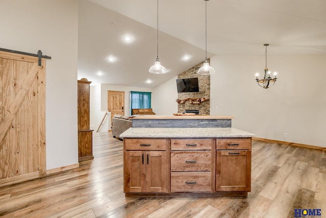 kitchen featuring a barn door, light stone counters, light hardwood / wood-style floors, and hanging light fixtures