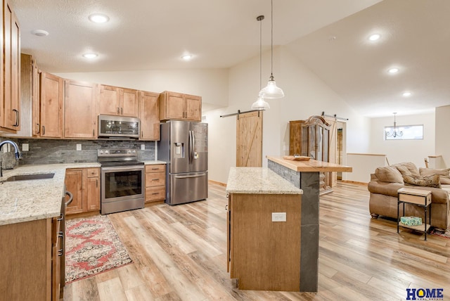 kitchen featuring appliances with stainless steel finishes, tasteful backsplash, sink, a barn door, and hanging light fixtures