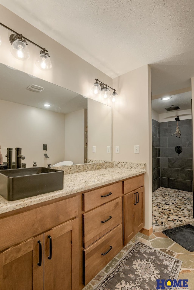 bathroom with tiled shower, a textured ceiling, and vanity