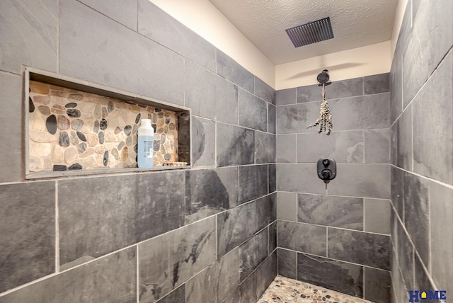 bathroom with tiled shower and a textured ceiling