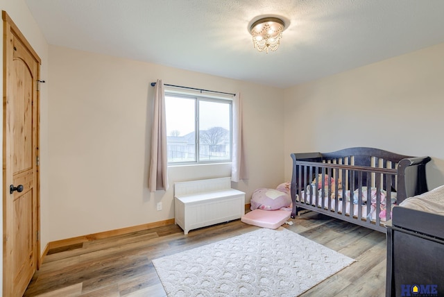 bedroom with light wood-type flooring and a nursery area