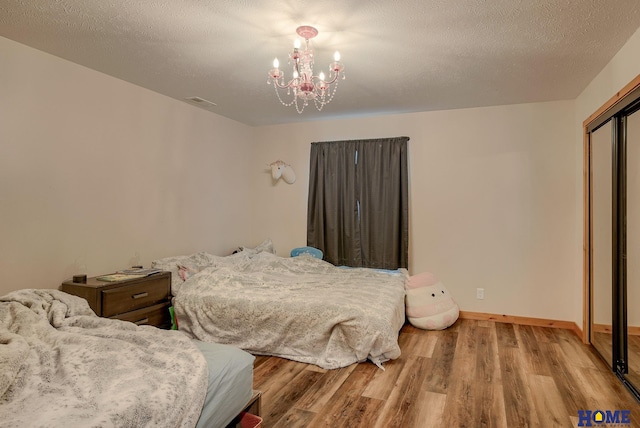 bedroom with a closet, a chandelier, a textured ceiling, and light wood-type flooring