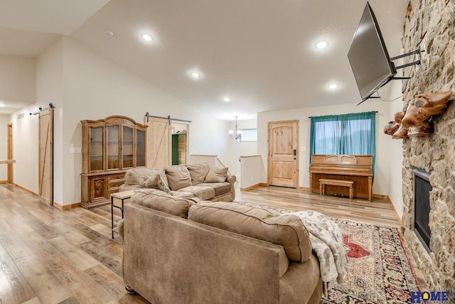 living room featuring a barn door, a fireplace, high vaulted ceiling, and light hardwood / wood-style flooring