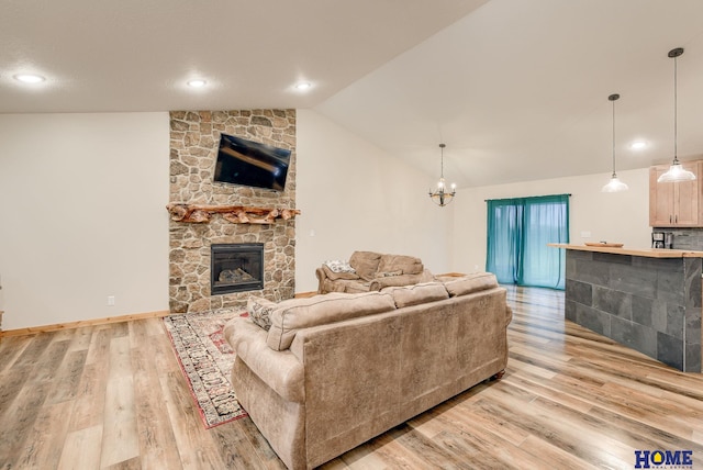 living room featuring an inviting chandelier, lofted ceiling, a fireplace, and light hardwood / wood-style flooring