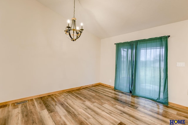 empty room featuring hardwood / wood-style floors, vaulted ceiling, and an inviting chandelier