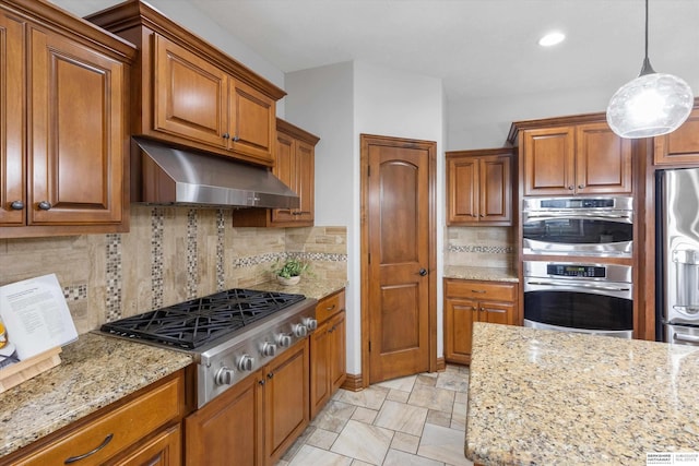 kitchen with appliances with stainless steel finishes, hanging light fixtures, backsplash, and light stone countertops