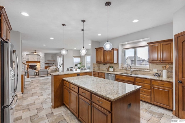 kitchen with a stone fireplace, stainless steel appliances, pendant lighting, a kitchen island, and sink