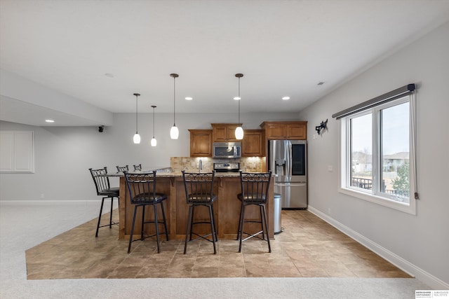 kitchen featuring stainless steel appliances, dark stone countertops, hanging light fixtures, a breakfast bar, and light colored carpet