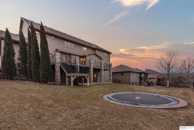 back house at dusk featuring a lawn, a wooden deck, and a trampoline