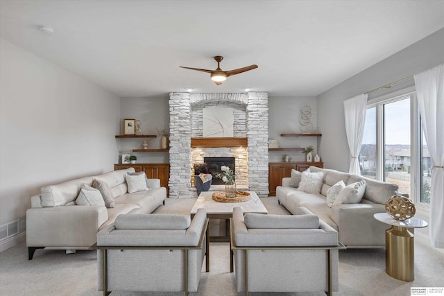 carpeted living room featuring ceiling fan and a stone fireplace