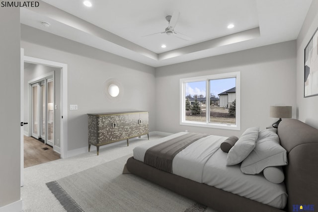 bedroom with ceiling fan, light carpet, and a tray ceiling