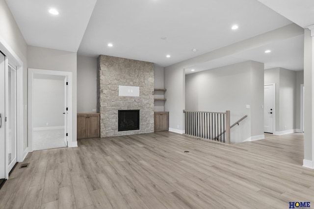 unfurnished living room with light hardwood / wood-style floors and a stone fireplace