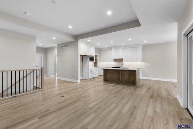 kitchen with white cabinetry, sink, a kitchen island with sink, decorative backsplash, and light wood-type flooring