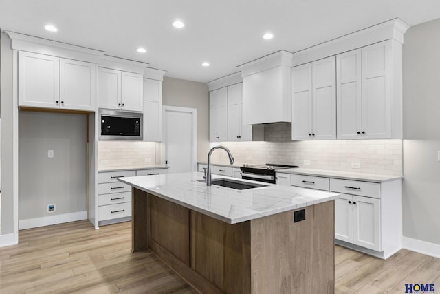 kitchen with custom range hood, built in microwave, a center island with sink, stainless steel stove, and white cabinetry