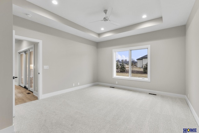 carpeted empty room featuring a raised ceiling and ceiling fan